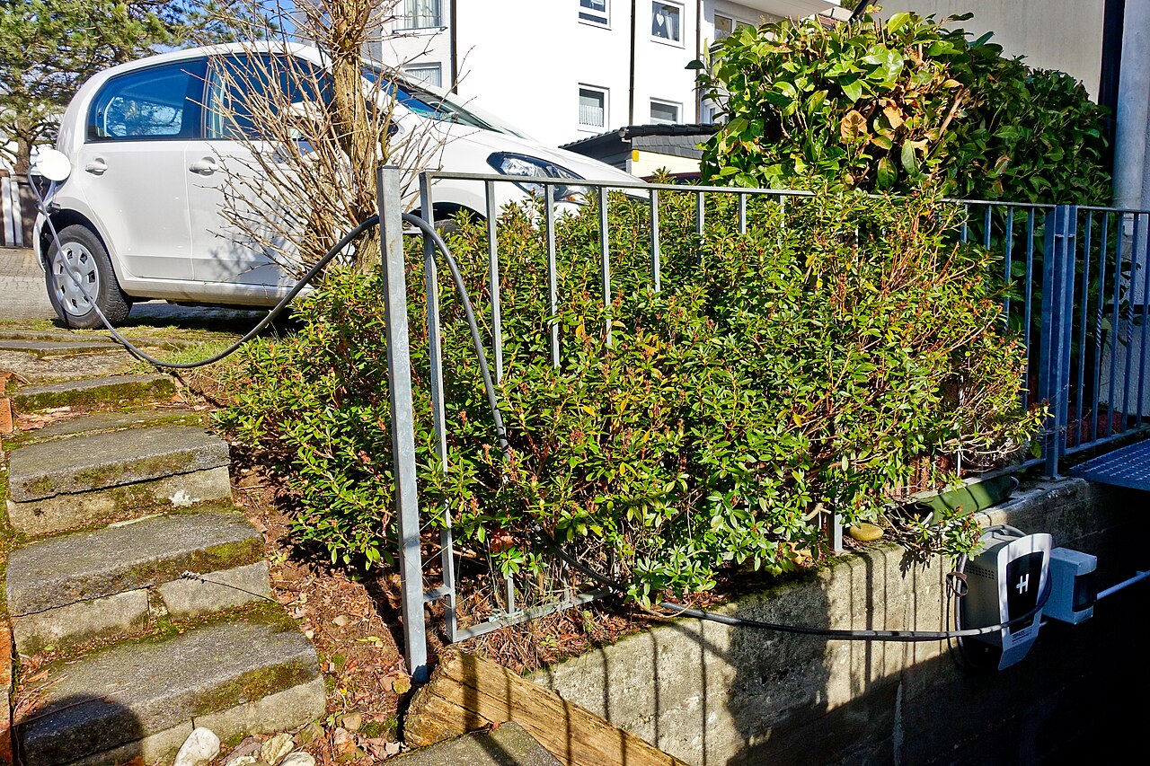 Wall-mounted charger on a house wall with a cable running to a small electric car