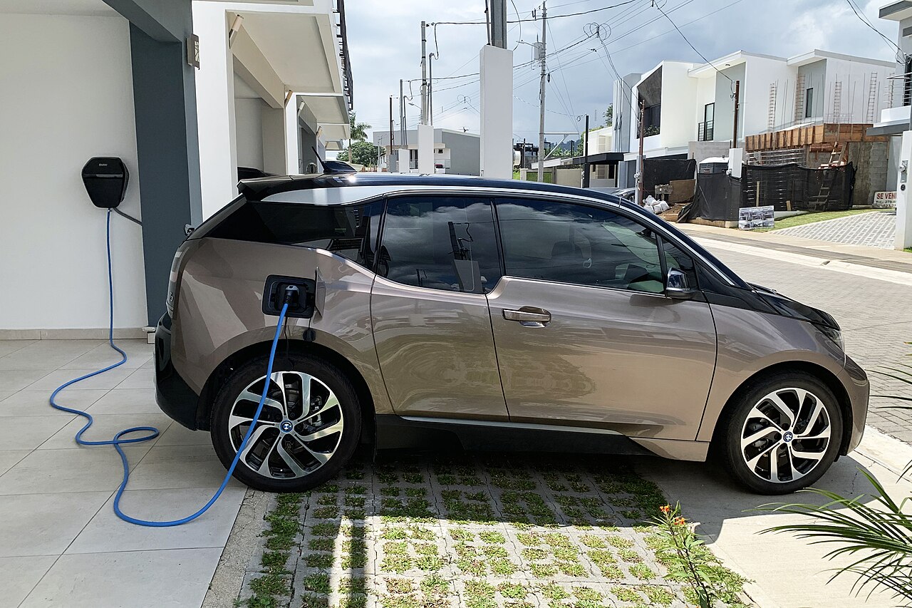 Small electric hatchback parked beside a house, connected to a wall-mounted charger