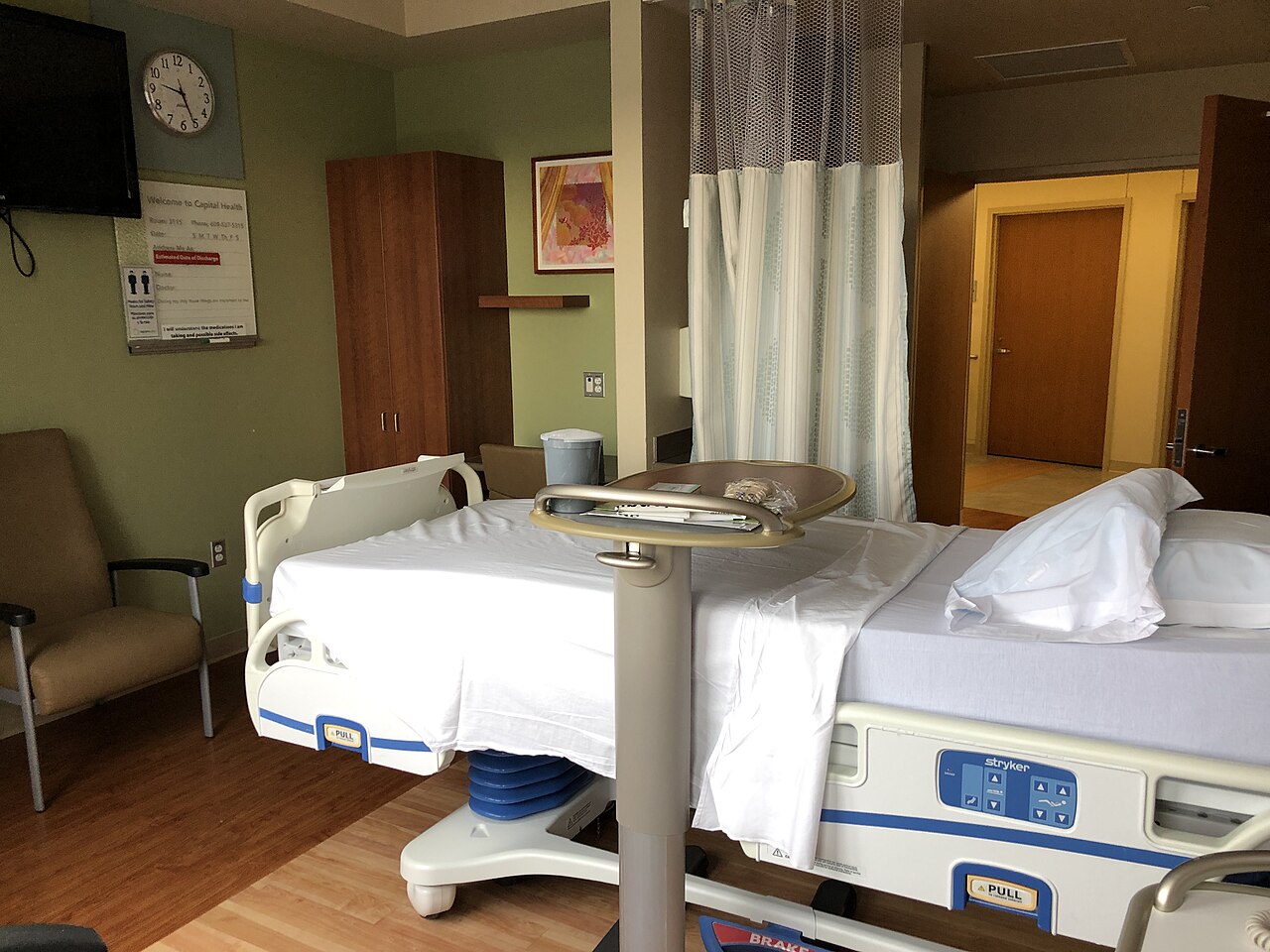 Empty hospital bed in a single recovery ward room with monitoring equipment on the wall
