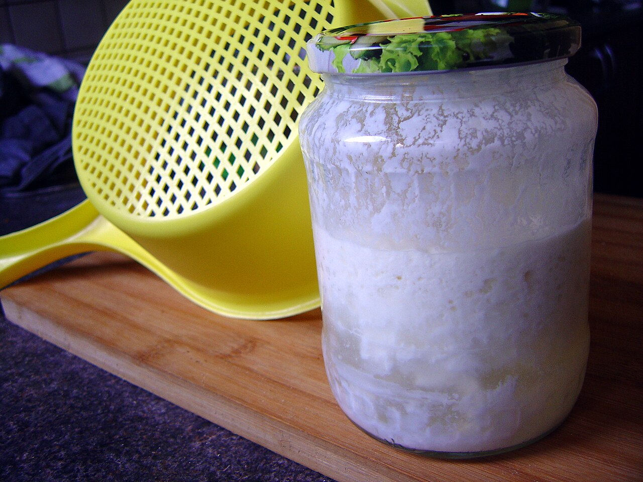 Home-made kefir in a jar with a plastic strainer used to separate the grains