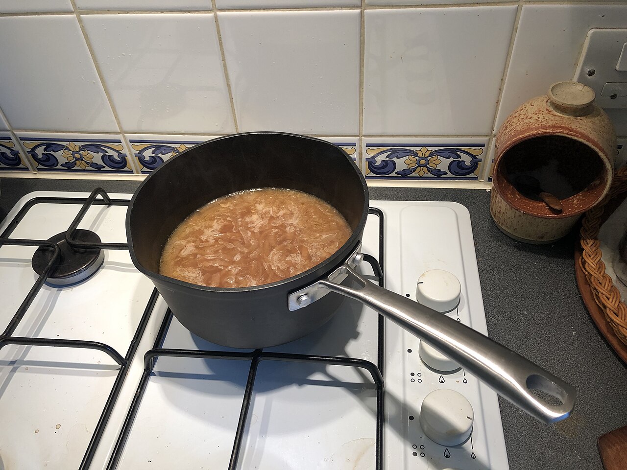 Non-stick saucepan of onion soup heating on a hob beside a salt pig