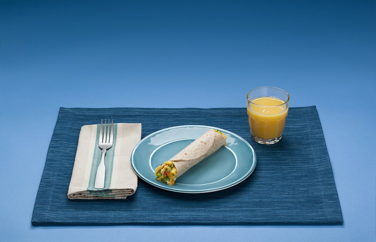 Breakfast plate with tortilla, scrambled eggs, cheese, vegetables and orange juice