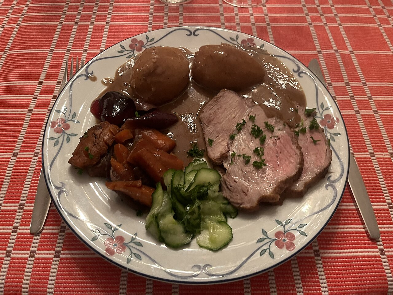 Plate of pork with potatoes, boiled vegetables, pickled cucumber and brown sauce