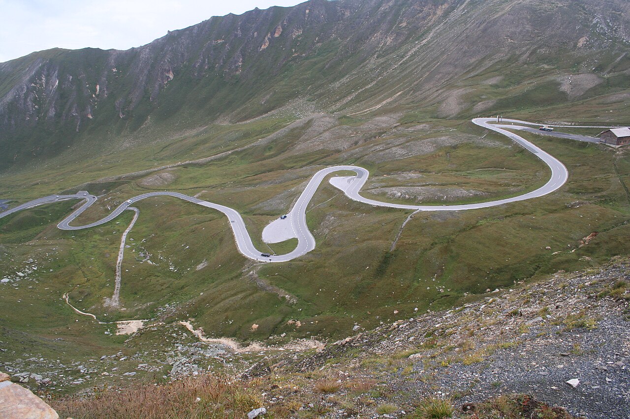 Mountain road curving across a bare alpine slope with peaks behind