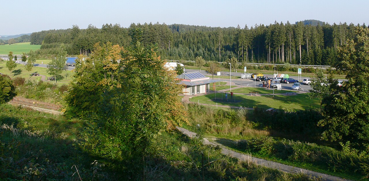 Motorway rest area seen from a slope above, with parking and planting