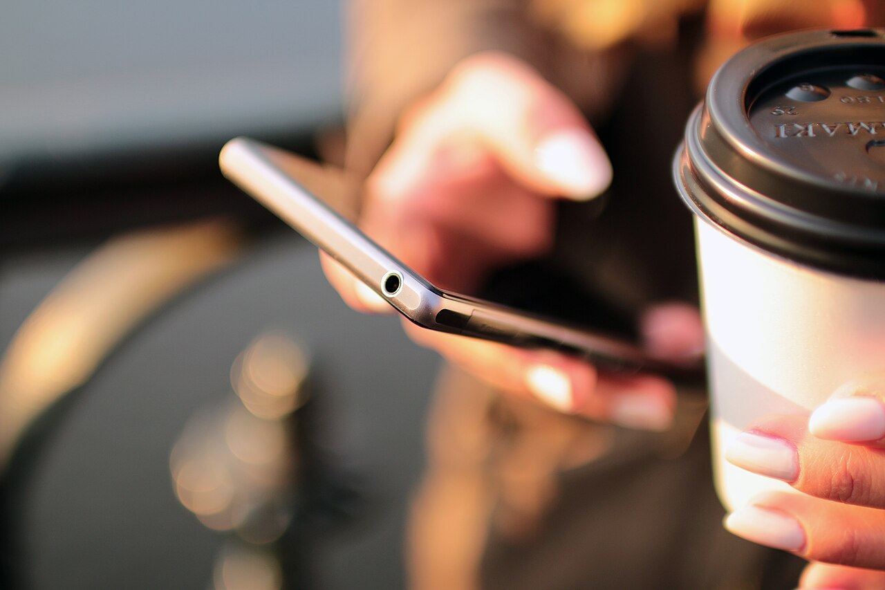 Hands holding a smartphone over a table beside a coffee cup