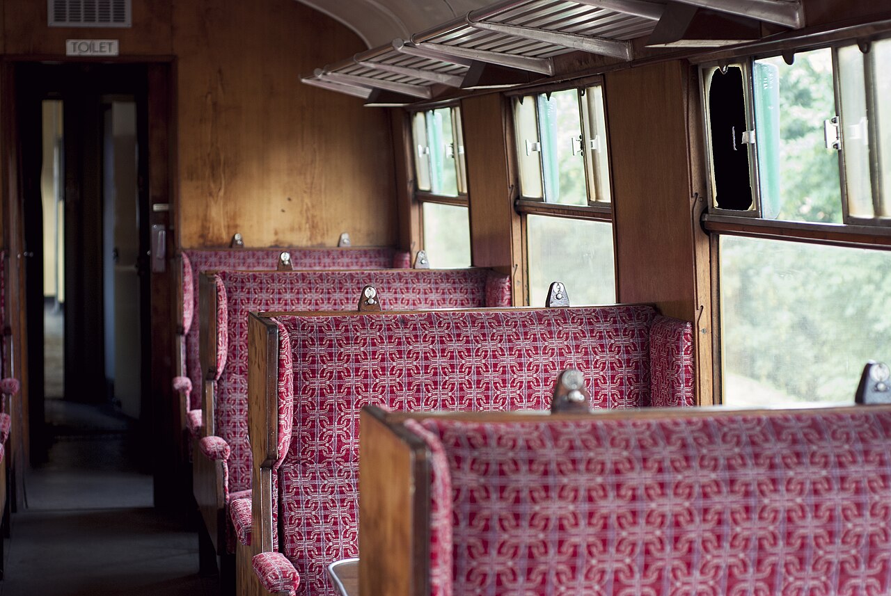 Interior dun vello vagón de ferrocarril británico con asentos tapizados en fronte e unha ventá