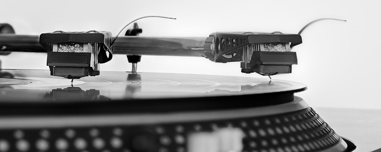 Tonearm and cartridge tracking the groove of a black record, shot in extreme close-up