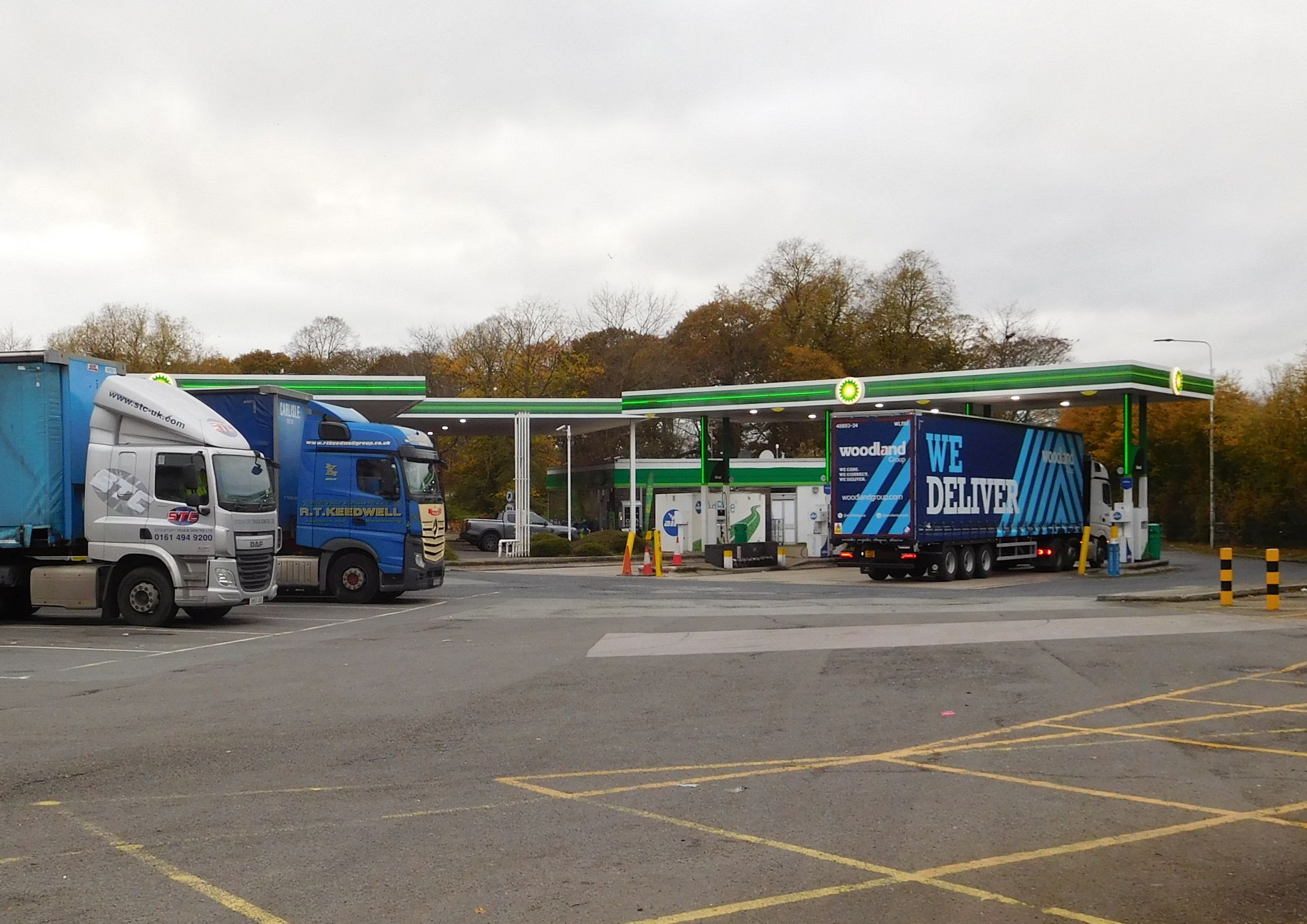 A motorway services forecourt on a grey day, with lorries parked beside the filling station canopy.